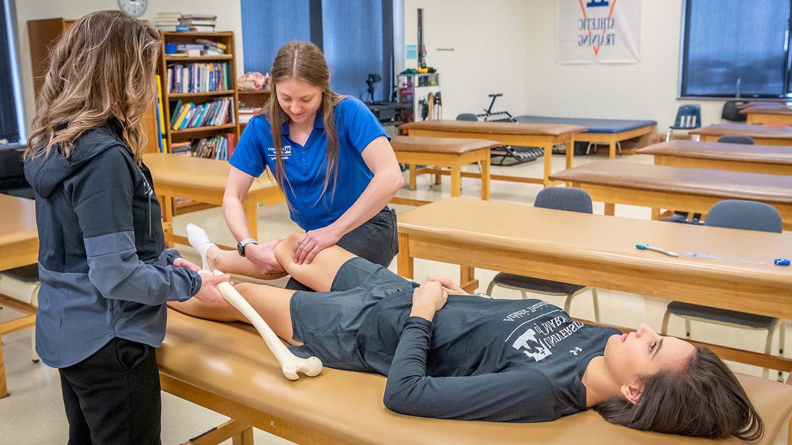 Athletic training student completing an assessment on athlete’s knee while instructor is watching
